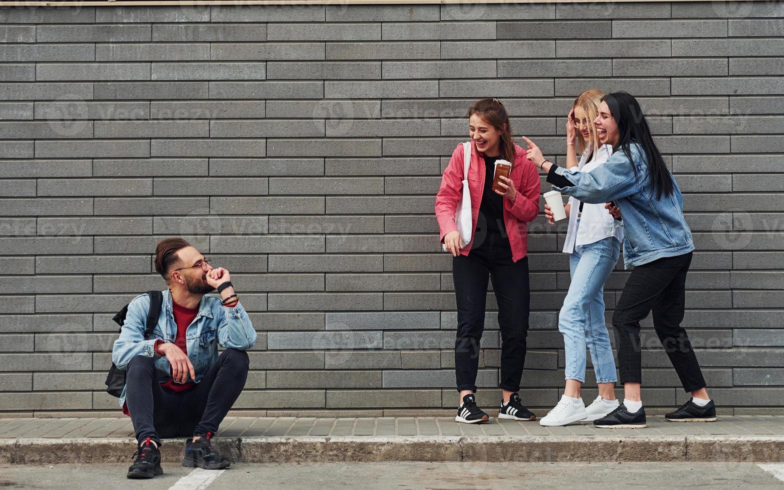 três mulheres de pé e rindo de um cara sentado ao ar livre perto de um prédio durante o dia foto