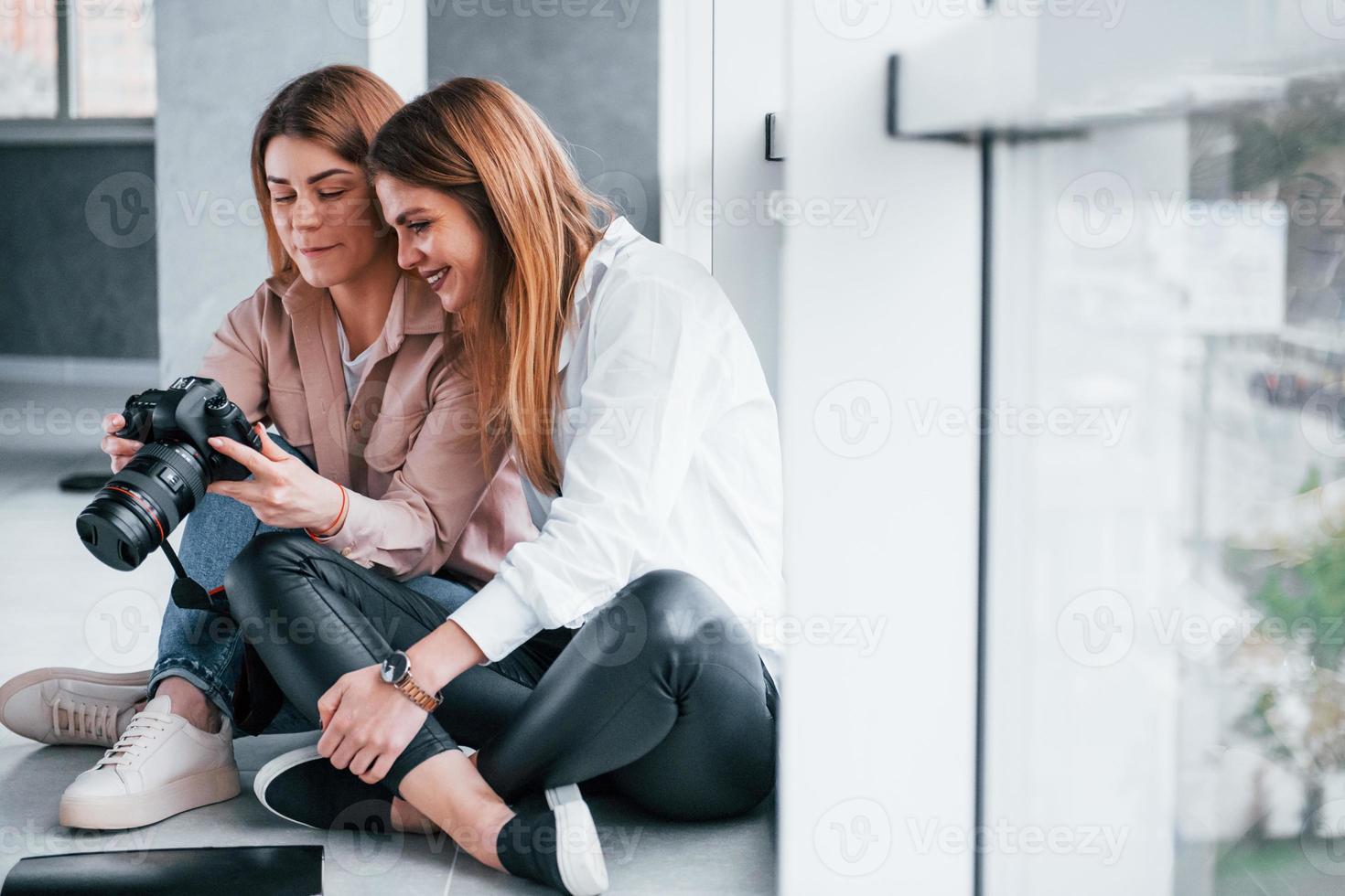 duas mulheres sentadas juntas dentro de casa e olham as fotos na câmera