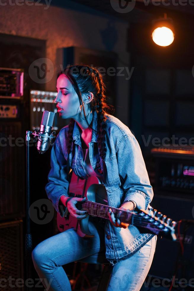 jovem bela artista feminina com violão cantando e ensaiando em um estúdio de gravação foto