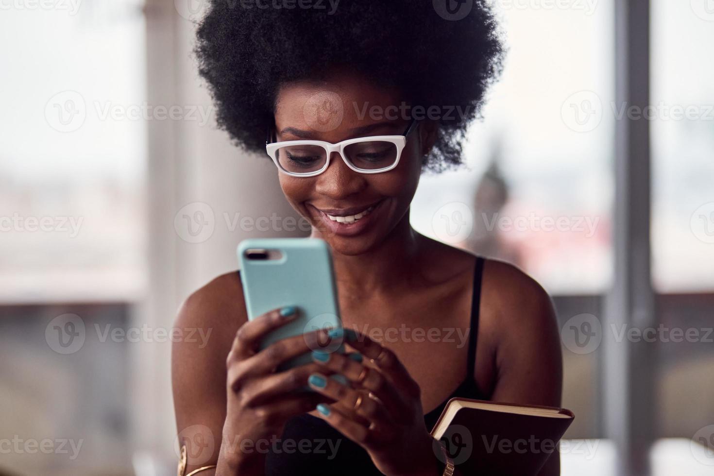 alegre mulher afro-americana segurando smartphone e bloco de notas foto