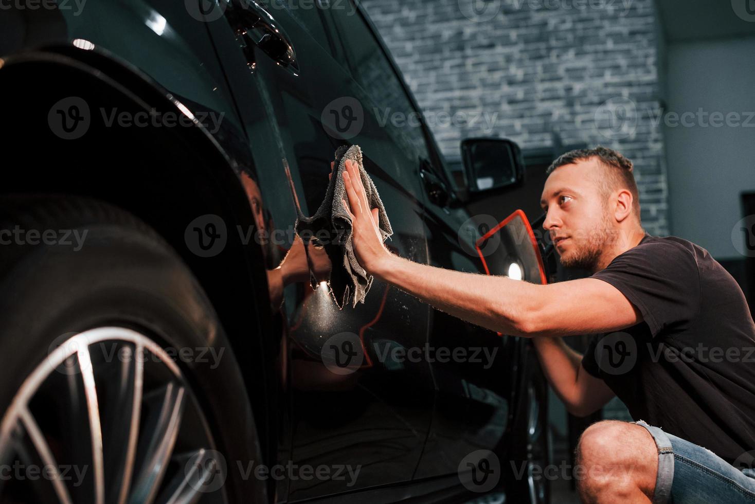 automóvel preto moderno é limpo pelo homem dentro da estação de lavagem de carros foto