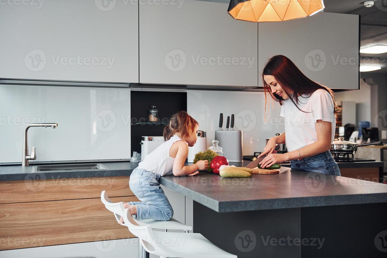 mãe com sua filha cortando legumes dentro de casa na cozinha foto