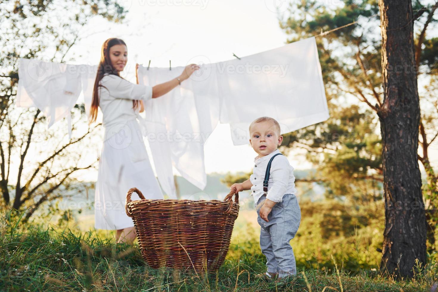 roupas limpas penduradas na corda para secar. jovem mãe com seu filho pequeno está ao ar livre na floresta. lindo sol foto