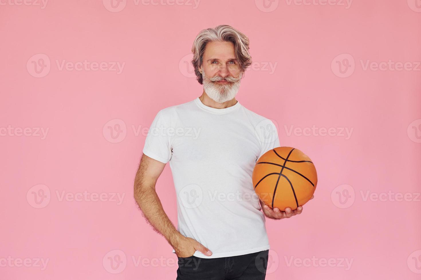 com bola de esporte nas mãos. elegante homem sênior moderno com cabelos grisalhos e barba está dentro de casa foto