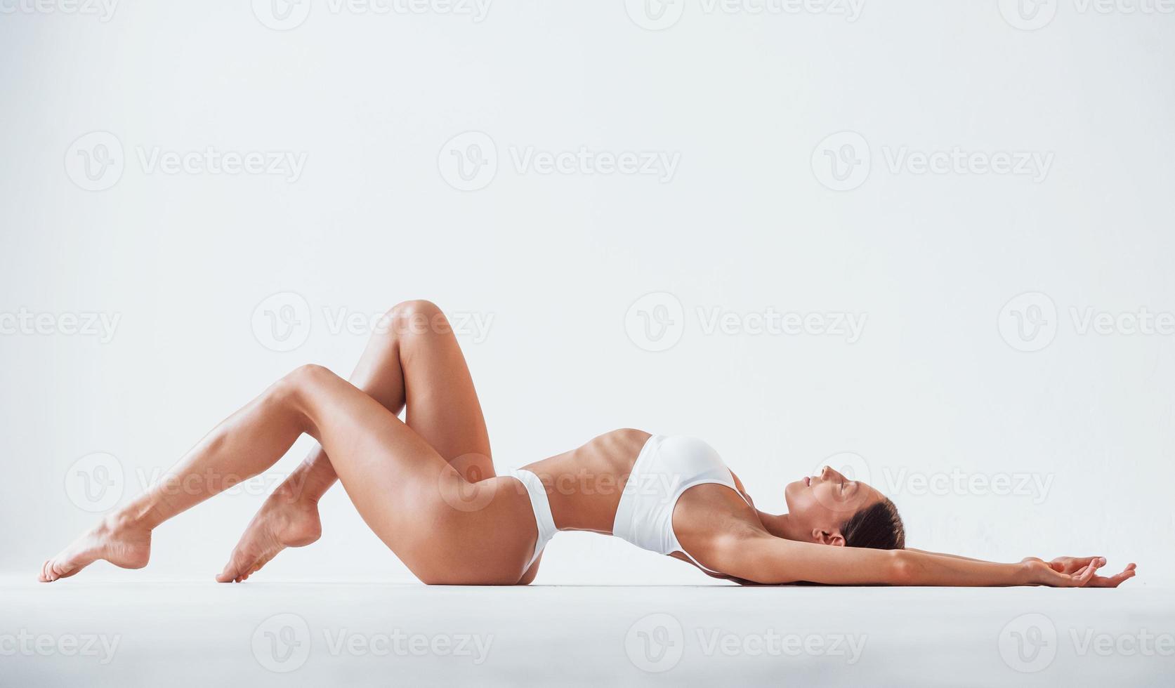 vista lateral da garota que está deitada. mulher bonita com corpo magro em cueca está no estúdio foto