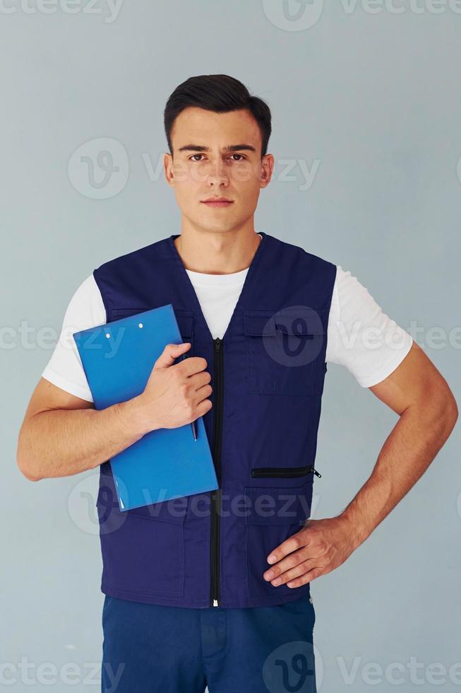 detém o bloco de notas. trabalhador do sexo masculino em pé uniforme azul dentro do estúdio contra fundo branco foto