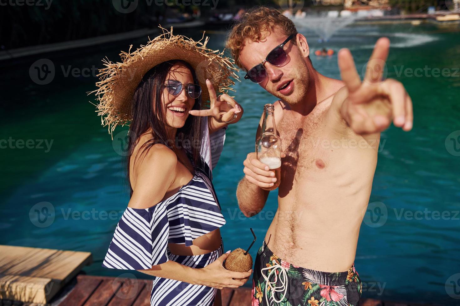 segurando bebidas nas mãos. casal alegre ou amigos juntos na piscina de férias foto