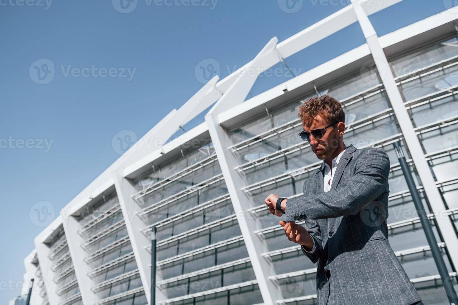 grande estádio atrás. jovem empresário em roupa formal cinza está ao ar livre na cidade foto