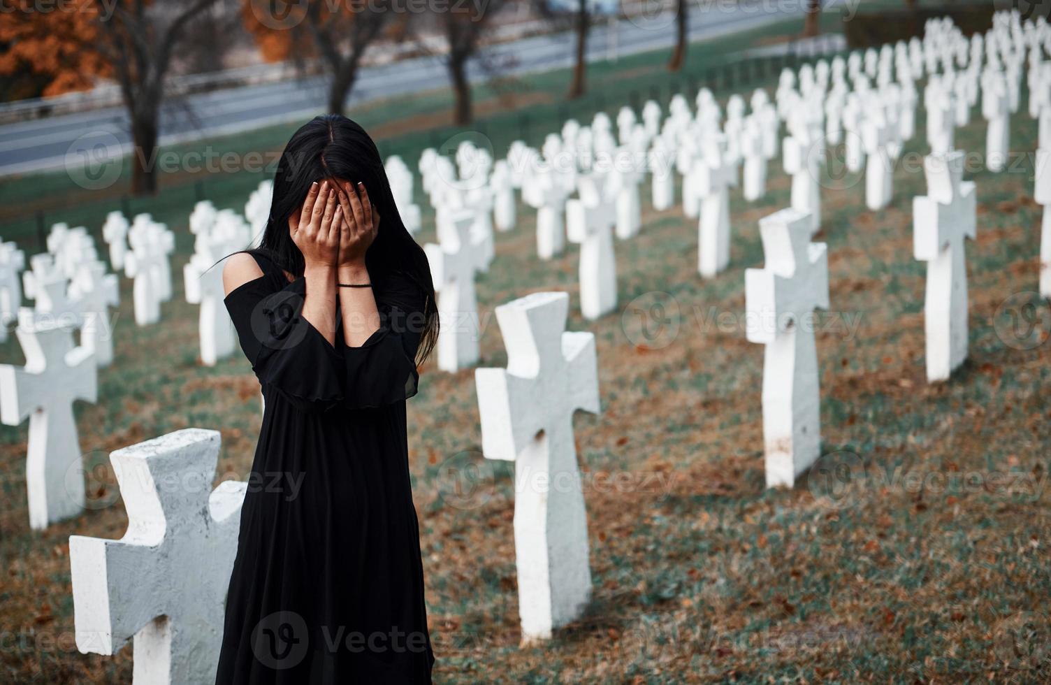 jovem mulher em roupas pretas, visitando o cemitério com muitas cruzes brancas. concepção de funeral e morte foto