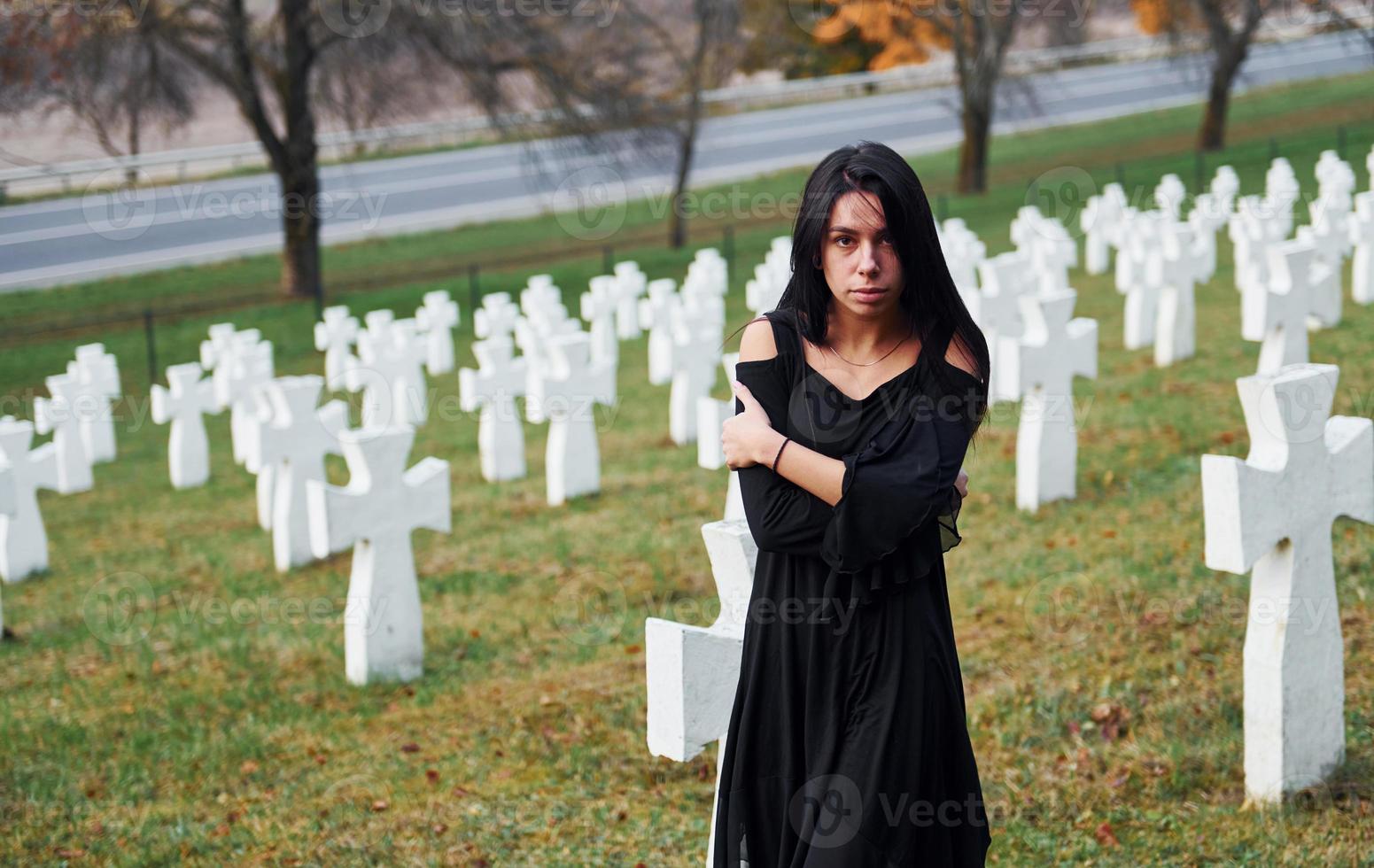 jovem mulher em roupas pretas, visitando o cemitério com muitas cruzes brancas. concepção de funeral e morte foto