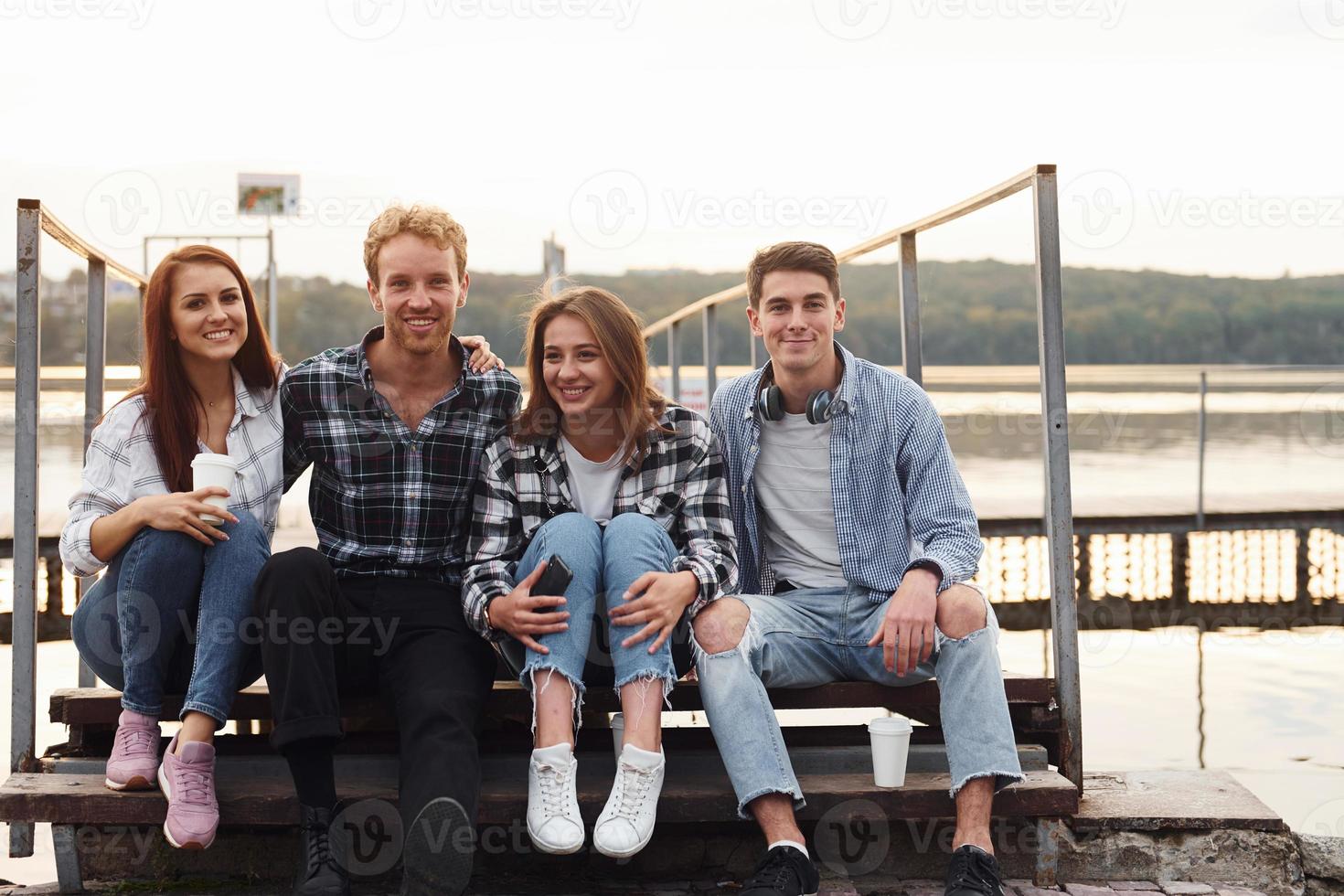 sentado perto do lago e se abraçando. grupo de jovens amigos alegres que está ao ar livre se divertindo juntos foto