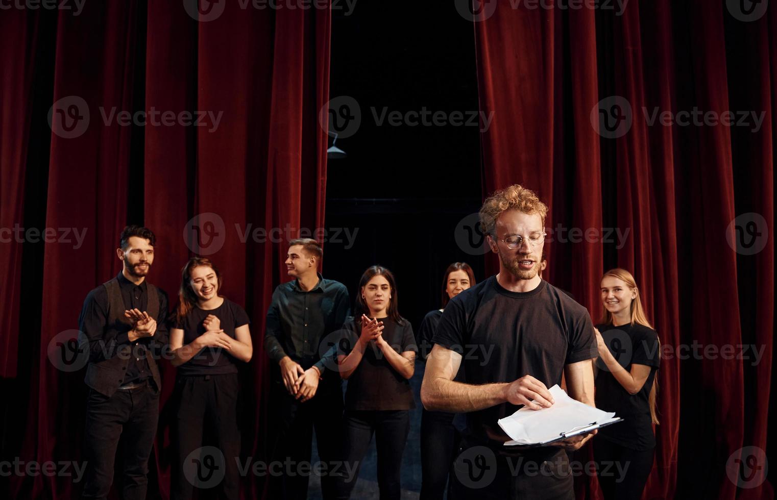 homem com bloco de notas pratica seu papel. grupo de atores em roupas de cor escura no ensaio no teatro foto