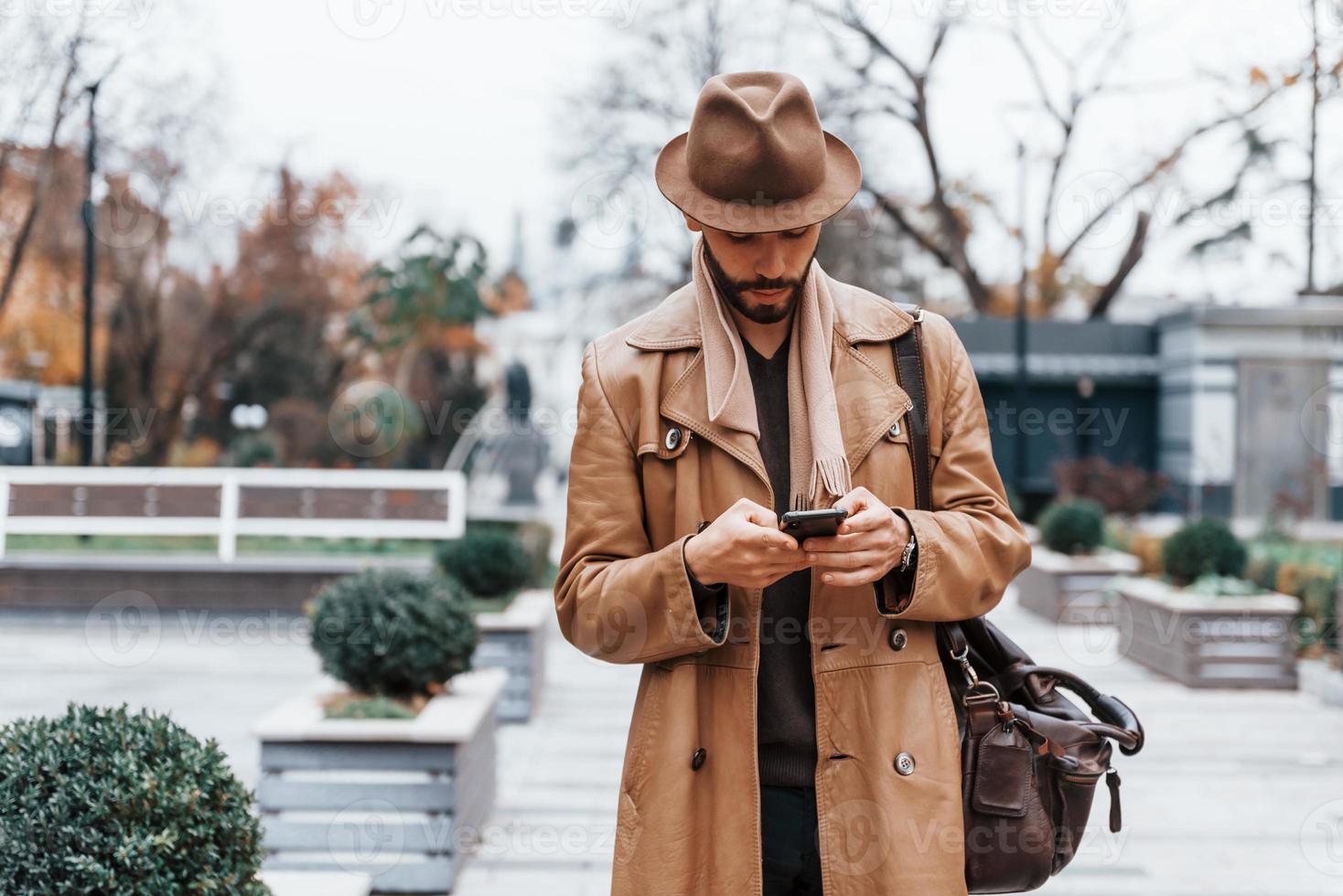 com saco. jovem modelo masculino em roupas da moda está ao ar livre na cidade durante o dia foto