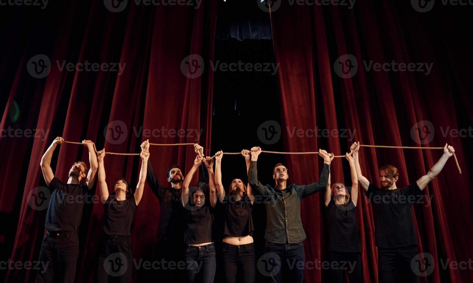 segurando a corda nas mãos acima das cabeças. grupo de atores em roupas de cor escura no ensaio no teatro foto