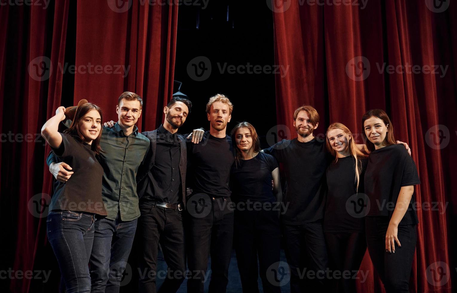 de pé contra cortinas vermelhas. grupo de atores em roupas de cor escura no ensaio no teatro foto