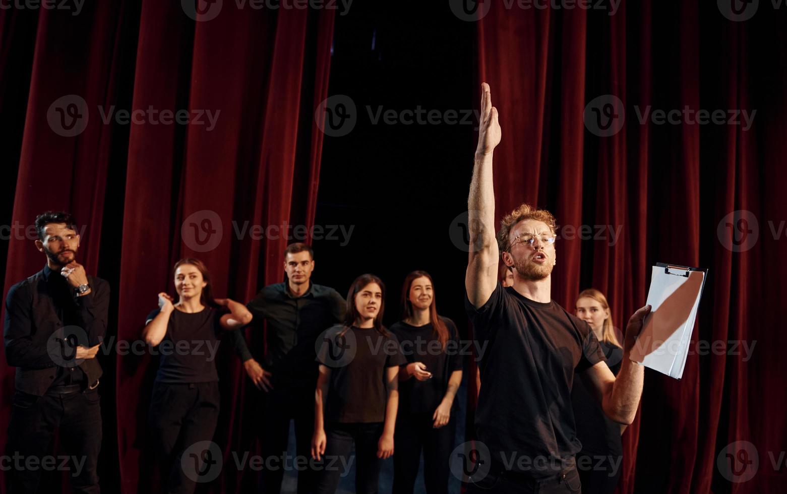 homem com bloco de notas pratica seu papel. grupo de atores em roupas de cor escura no ensaio no teatro foto