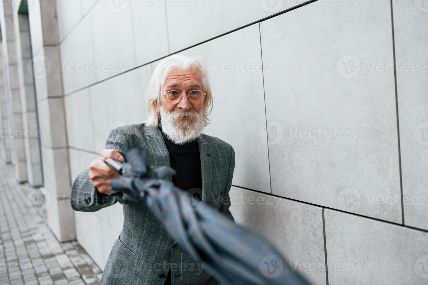 segura guarda-chuva. empresário sênior em roupas formais, com cabelos grisalhos e barba está ao ar livre foto