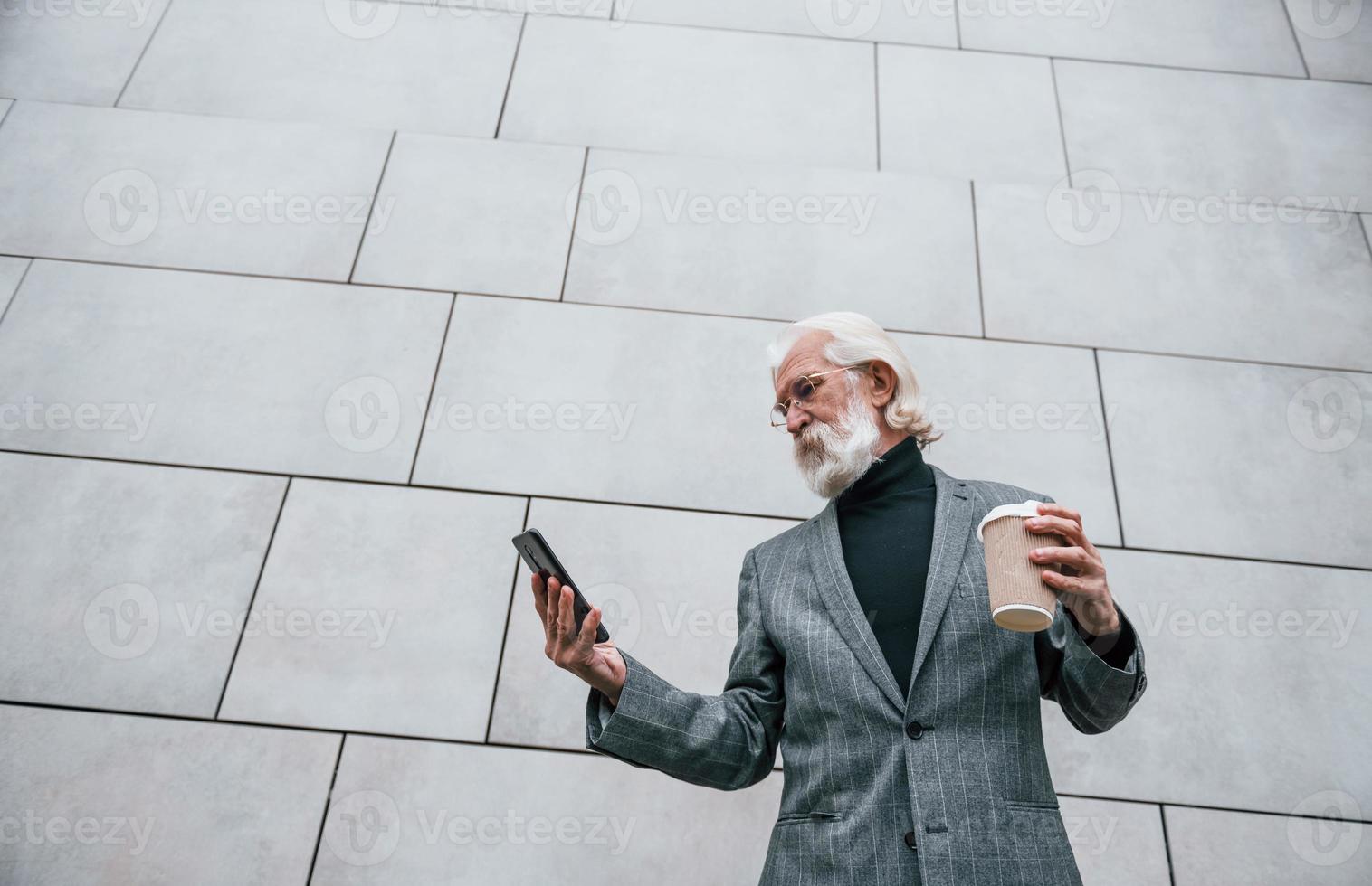 usando smartphones. empresário sênior em roupas formais, com cabelos grisalhos e barba está ao ar livre foto