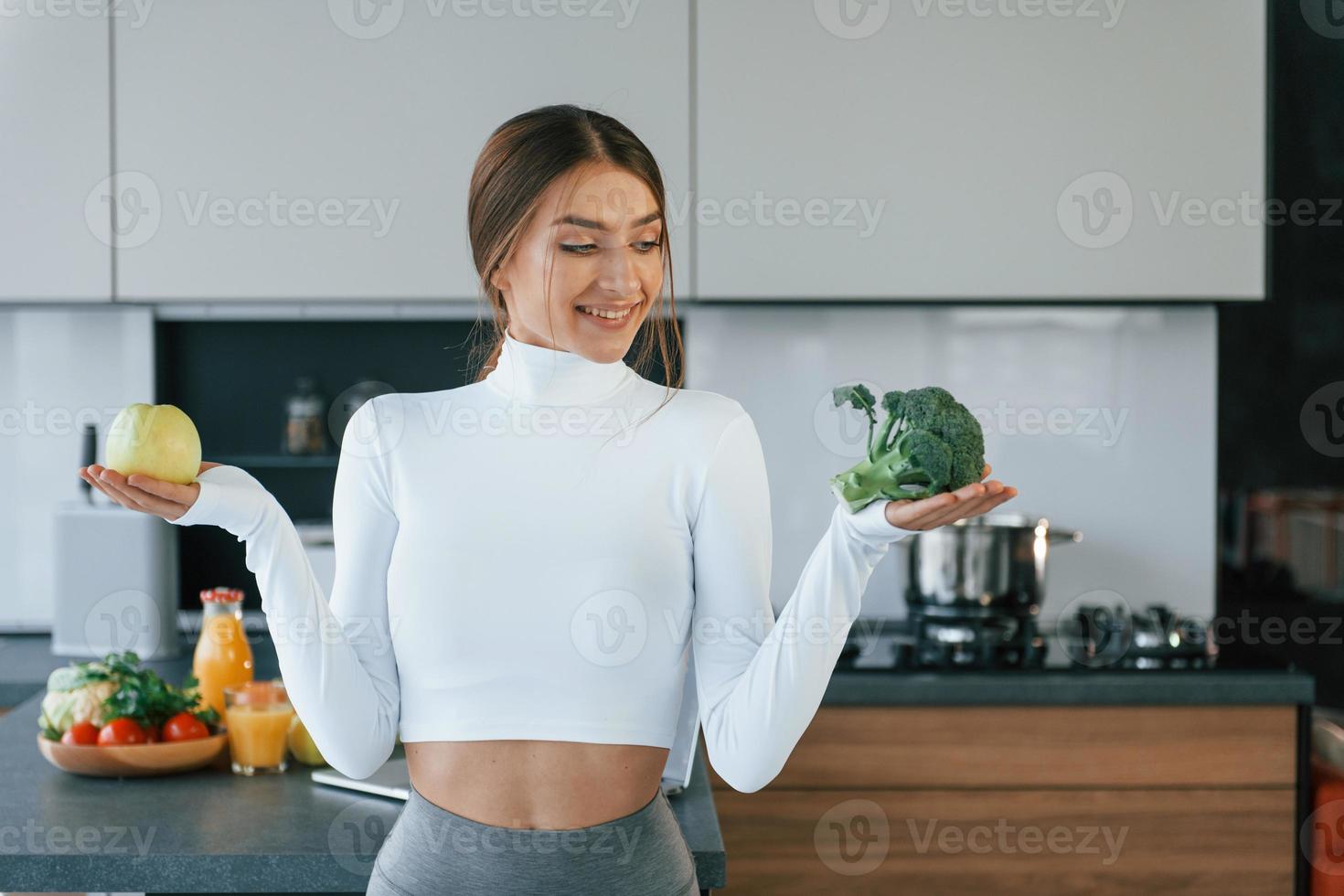 posa para uma câmera com legumes. jovem europeia está dentro de casa na cozinha dentro de casa com comida saudável foto