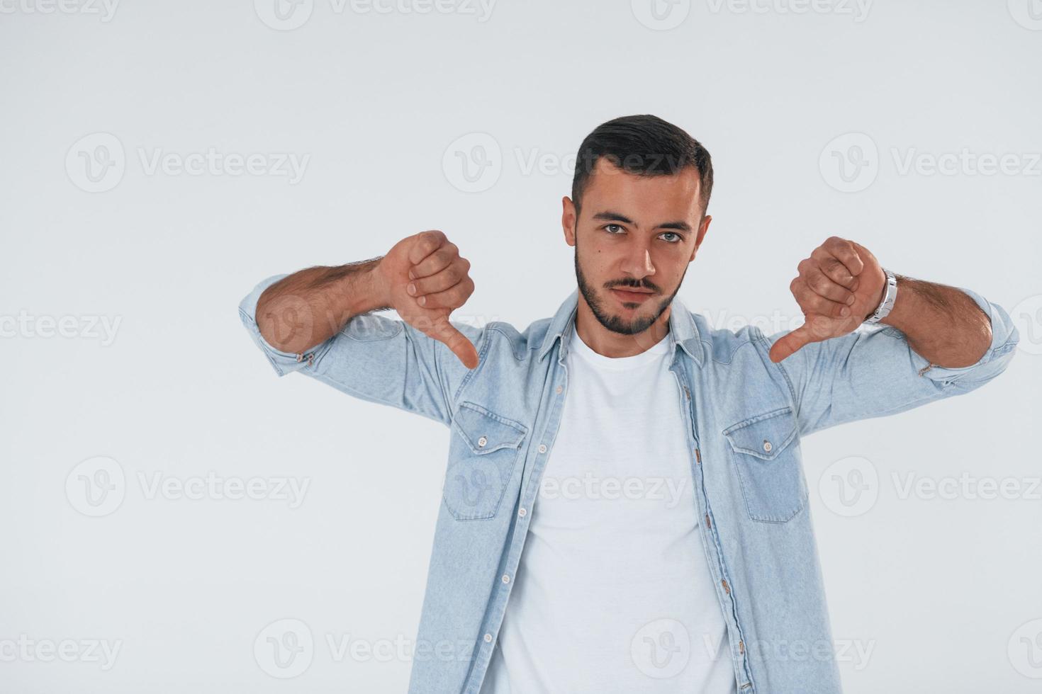 polegares para baixo. jovem bonito em pé dentro de casa contra um fundo branco foto