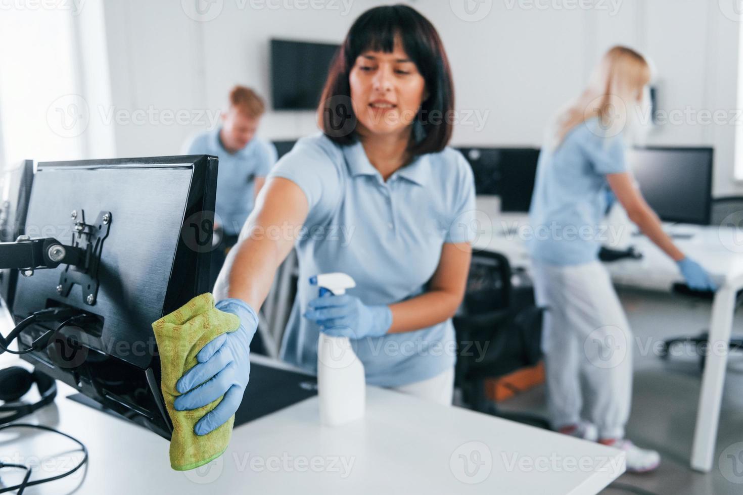 limpa monitor. grupo de trabalhadores limpa escritório moderno juntos durante o dia foto