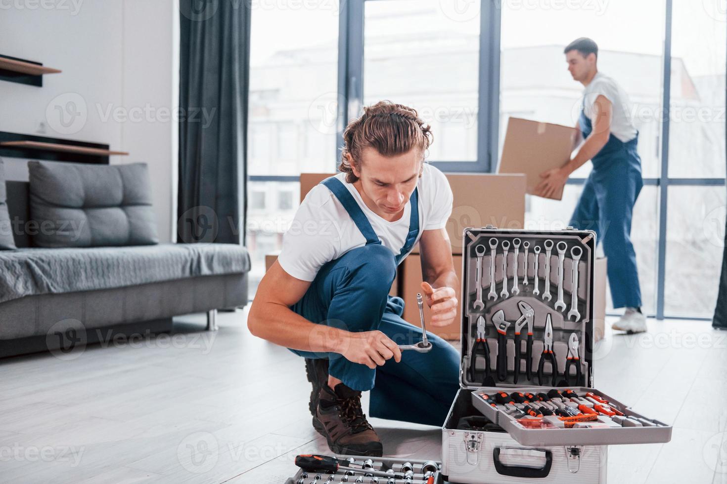 caso com equipamento. dois jovens em uniforme azul trabalhando dentro de casa na sala foto