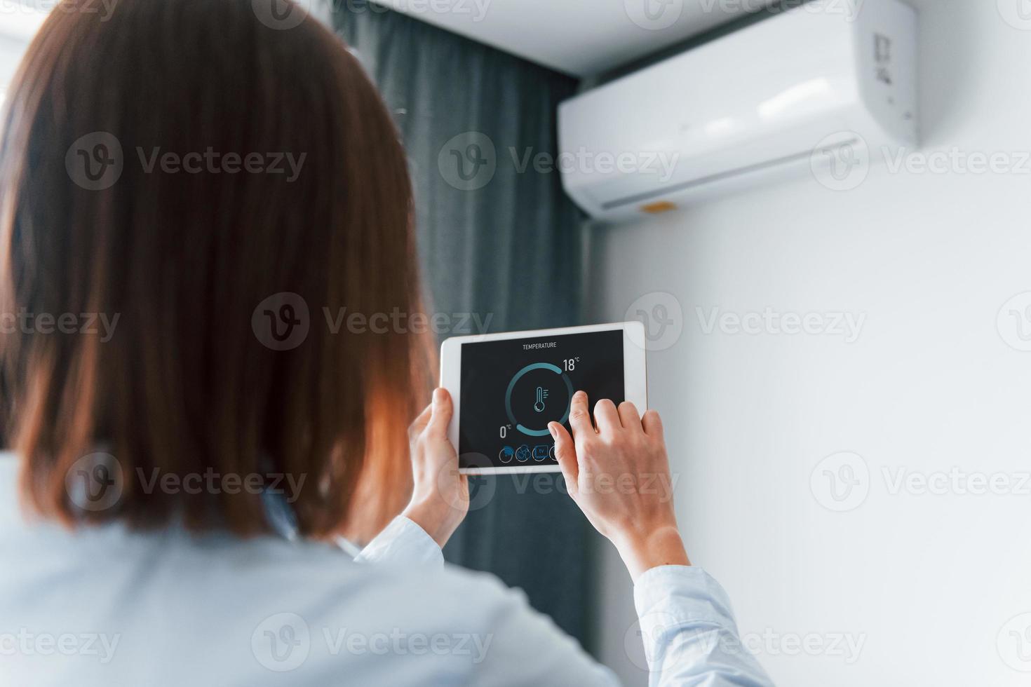 visão traseira da mulher que está dentro de casa controlando a tecnologia de casa inteligente foto