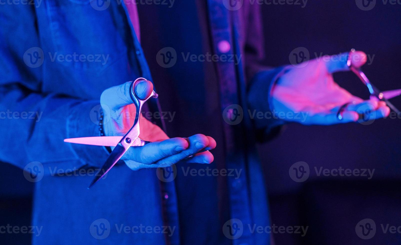 vista de perto das mãos do barbeiro que seguram uma tesoura. iluminação neon foto