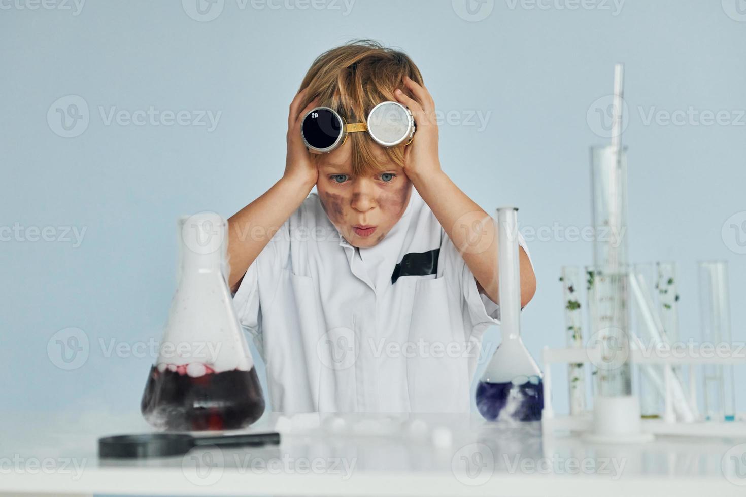 garotinho assustado de casaco brincando de cientista em laboratório usando equipamentos foto