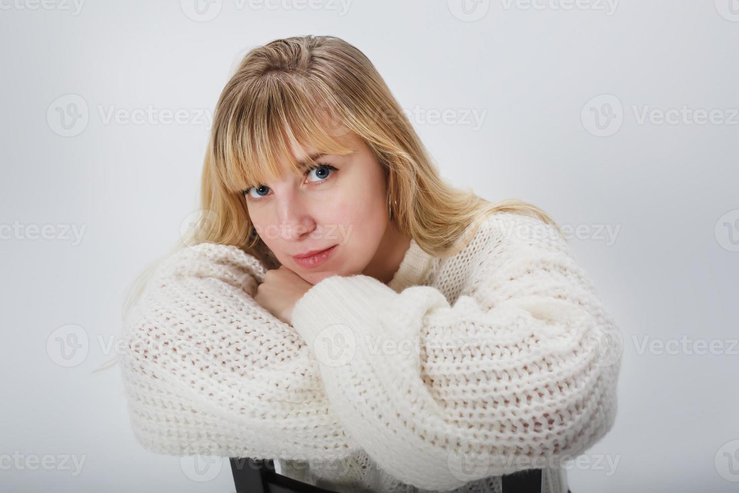 feche o retrato do modelo de menina loira em suéter de lã branca sobre fundo branco no estúdio foto