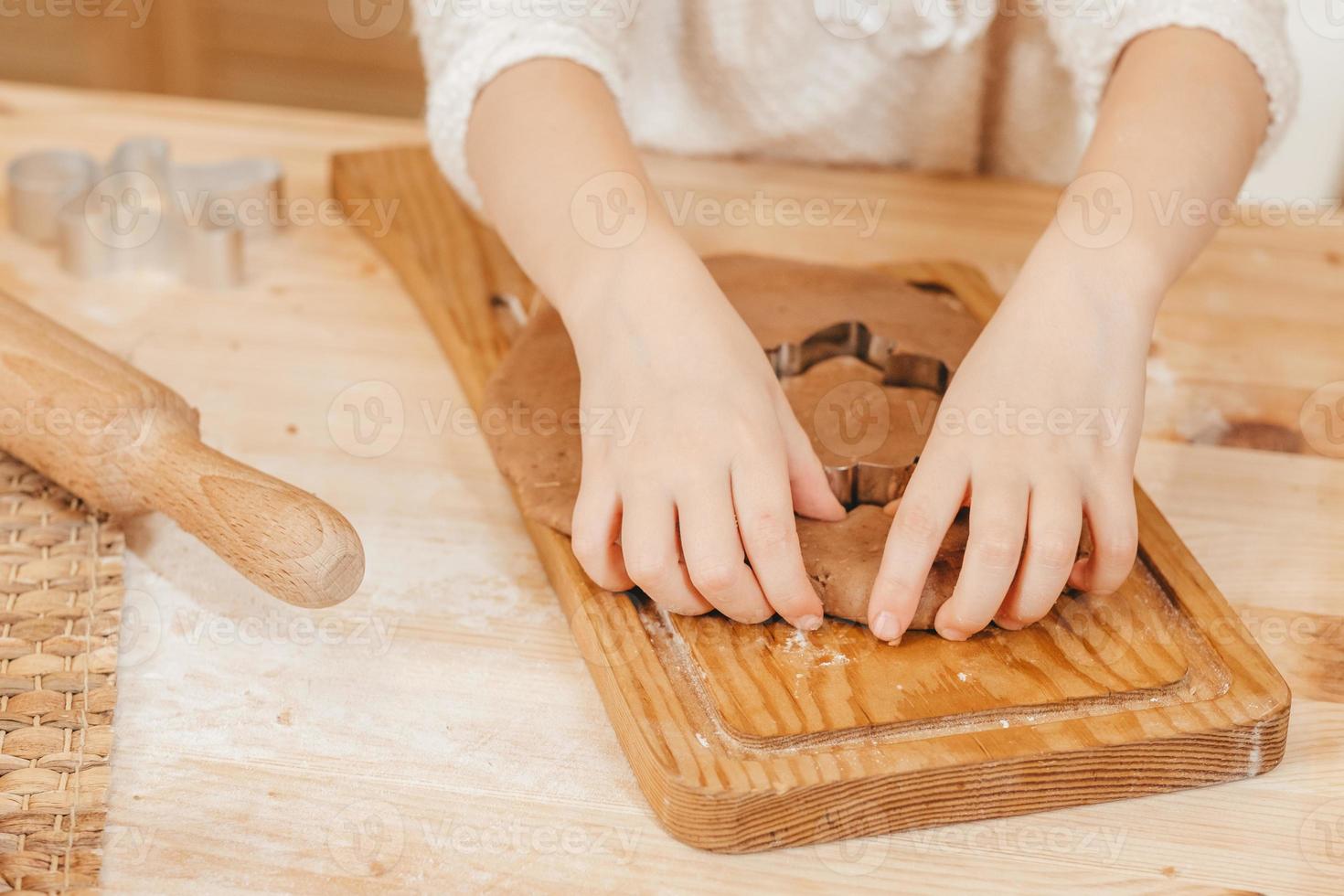 as mãos das crianças esculpem biscoitos na massa de pão de gengibre das estatuetas. menina preparando biscoitos de natal em uma mesa de madeira foto