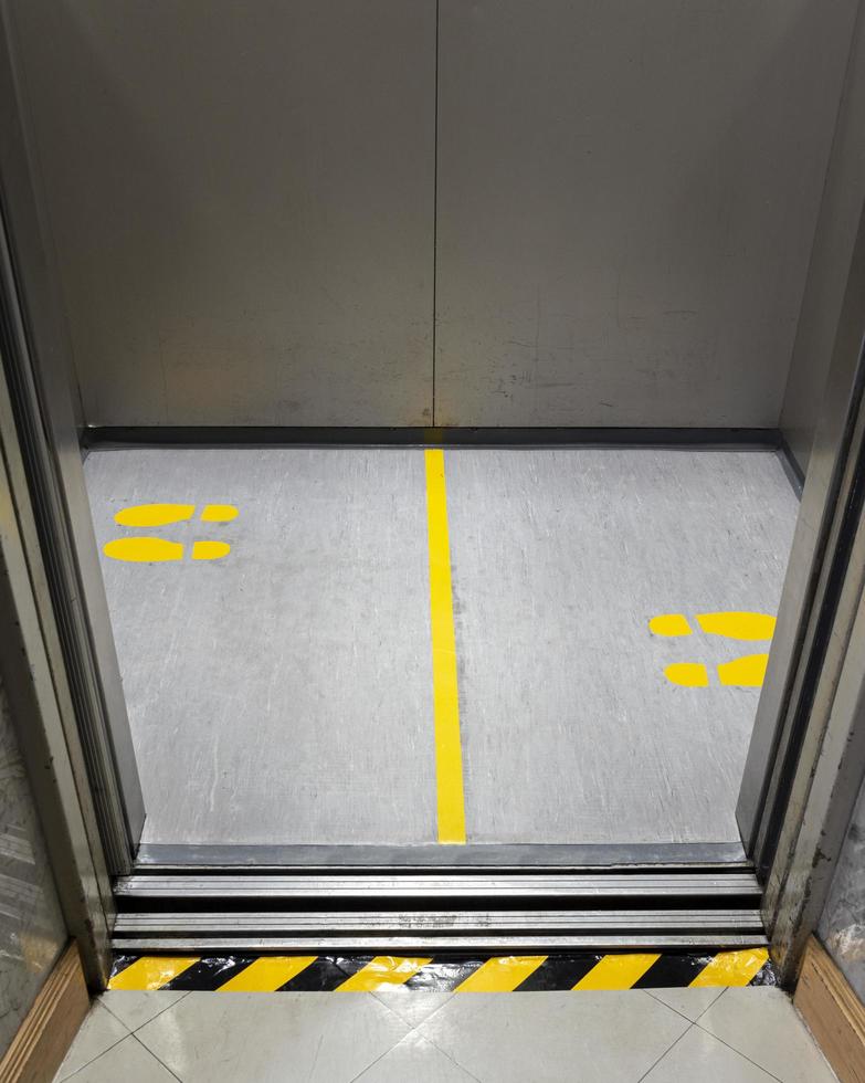 distanciamento social para covid-19 com placa de pegada amarela em elevador público foto