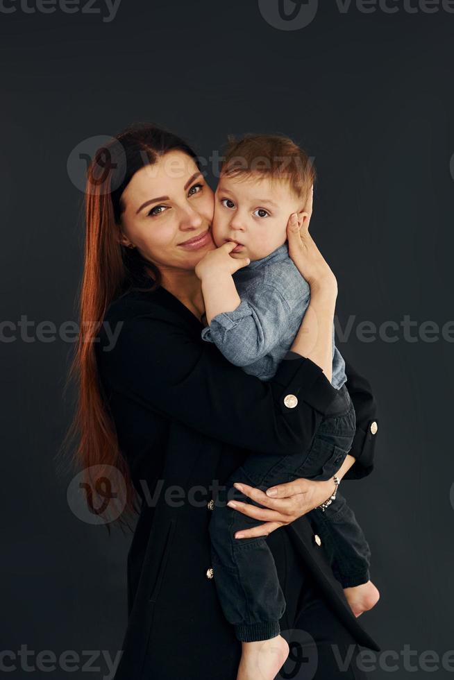 mãe em elegantes roupas pretas está com seu filho no estúdio foto