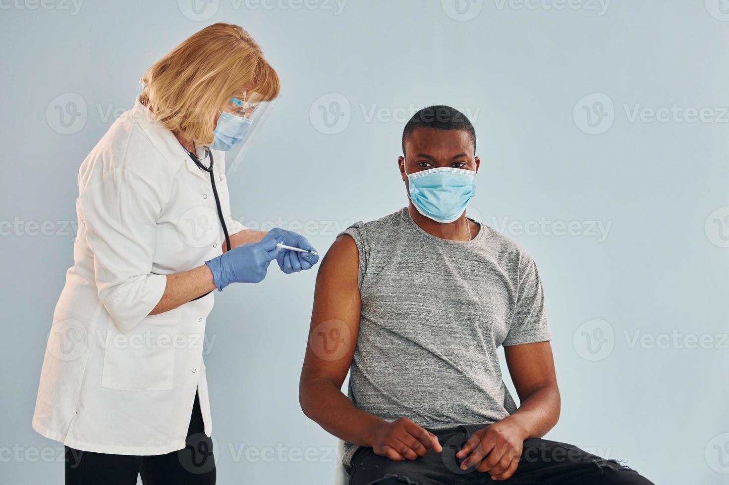 médico sênior dando injeção para jovem afro-americano no hospital foto