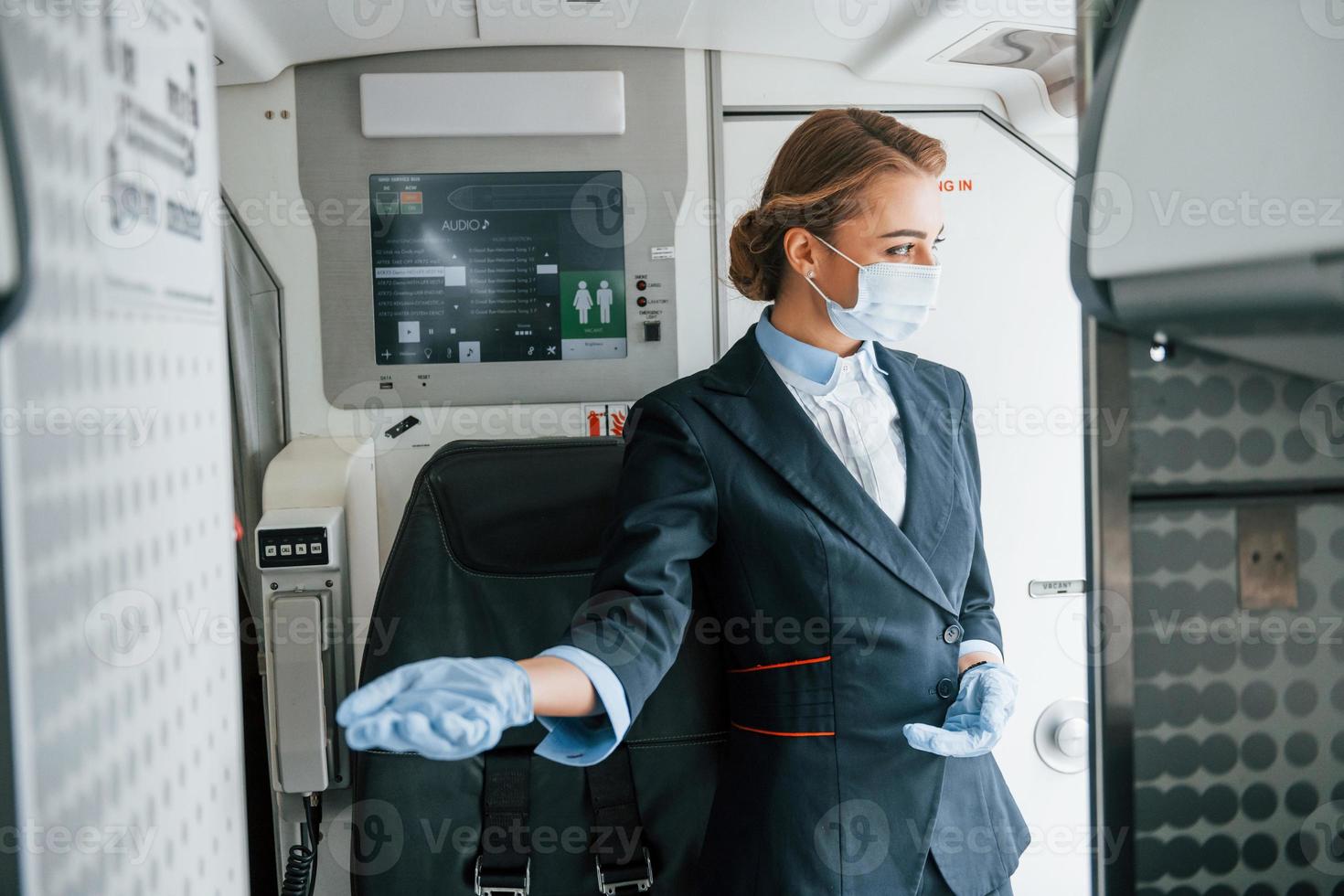 em luvas de proteção e máscara. jovem aeromoça no trabalho no avião de passageiros foto