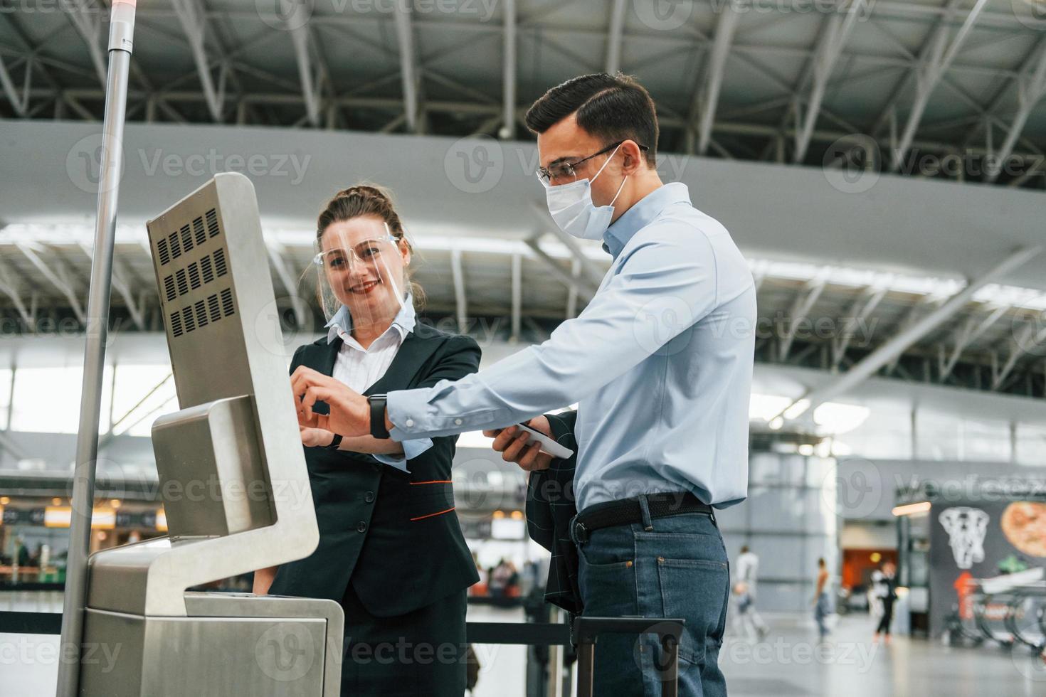 funcionário ajudando usando o terminal. jovem empresário em roupas formais está no aeroporto durante o dia foto