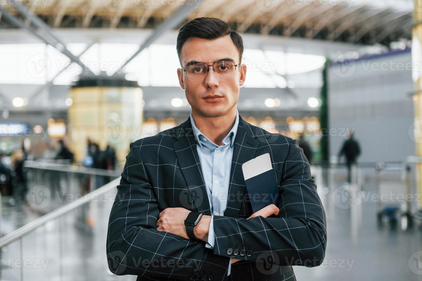 com os braços cruzados. jovem empresário em roupas formais está no aeroporto durante o dia foto