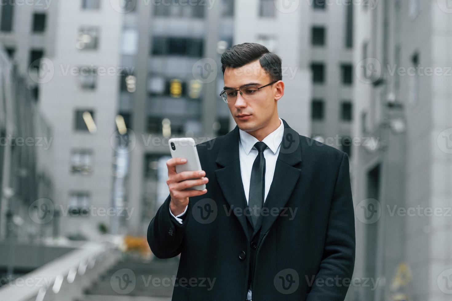 com smartphone. empresário de terno preto e gravata está ao ar livre na cidade foto