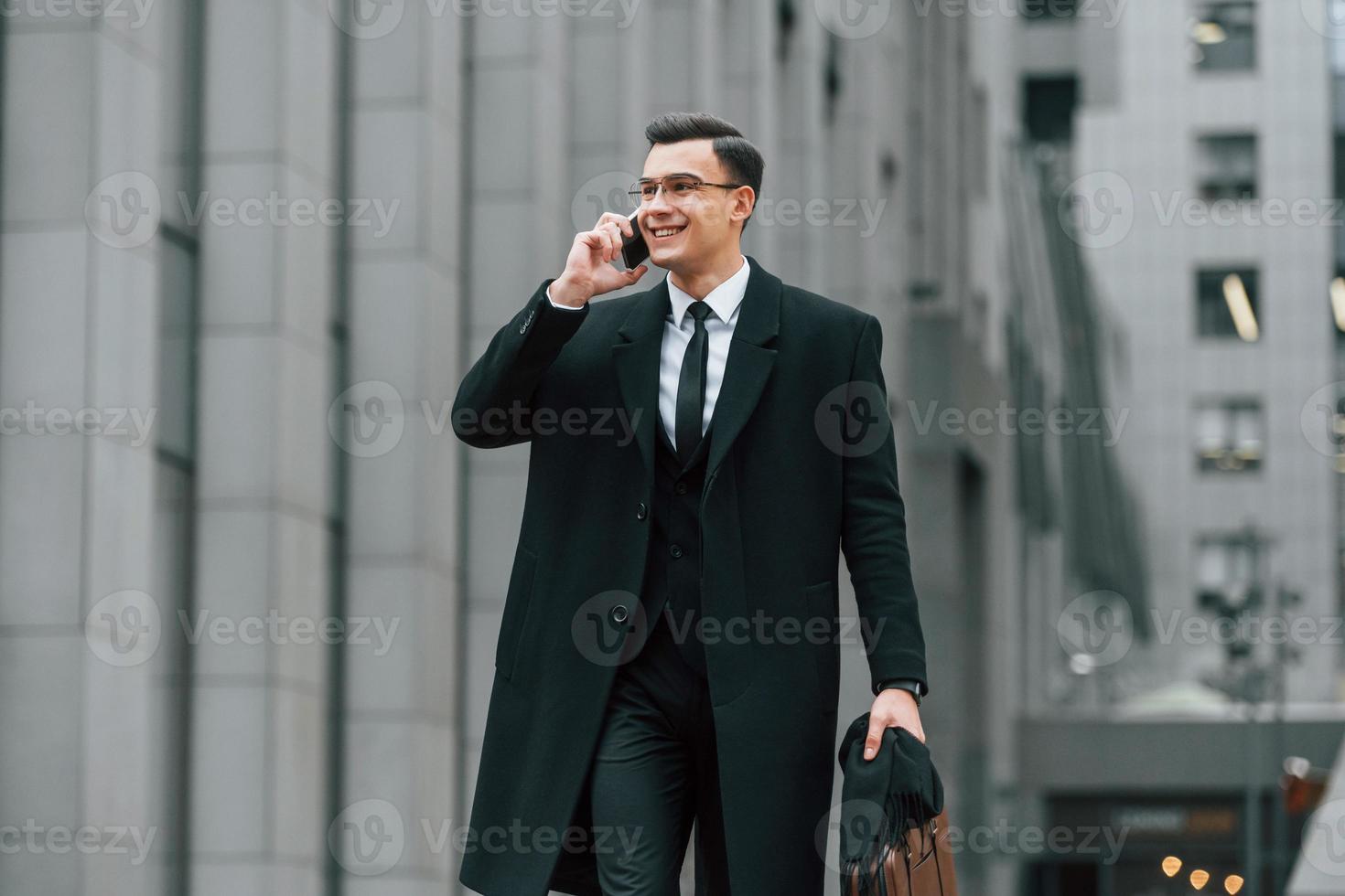 com smartphone. empresário de terno preto e gravata está ao ar livre na cidade foto