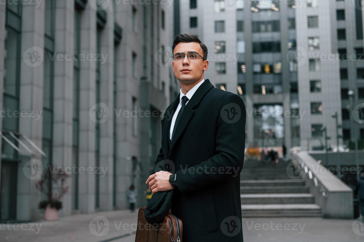 vista frontal. empresário de terno preto e gravata está ao ar livre na cidade foto