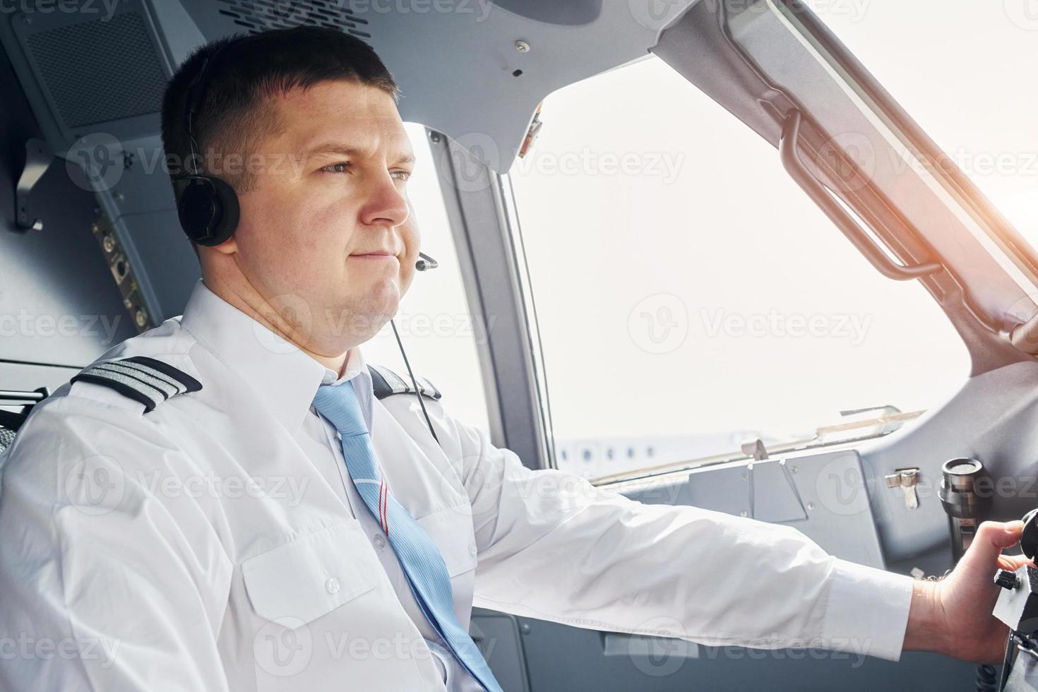 vista lateral. piloto com roupa formal senta-se no cockpit e controla o avião foto