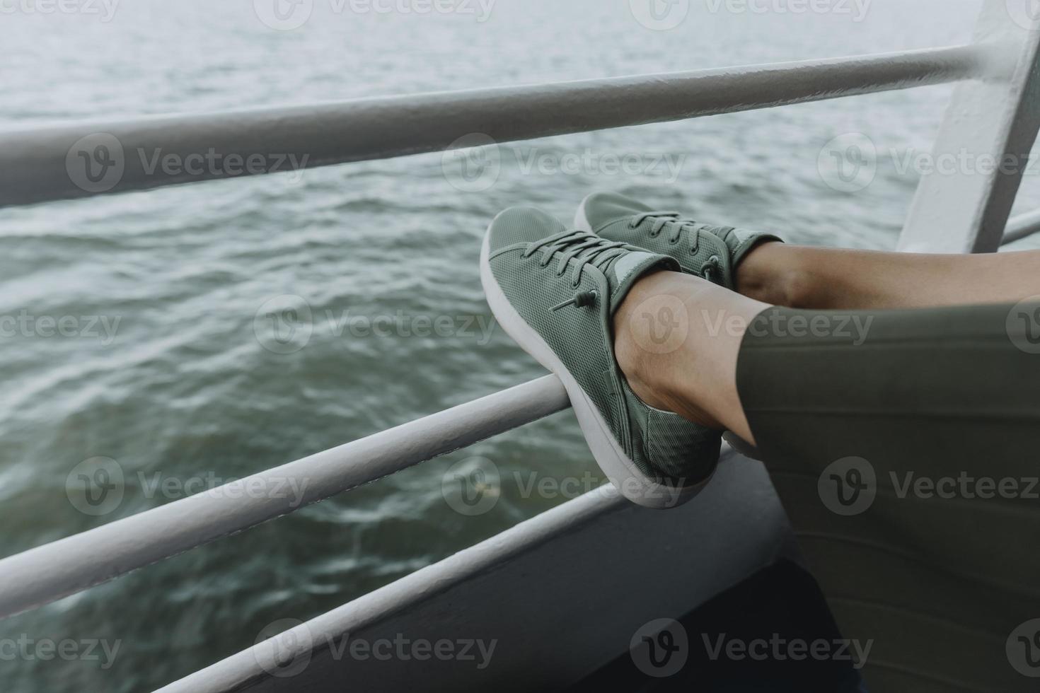 detalhe das pernas da mulher em tênis verde e saia verde descansando na grade da balsa foto