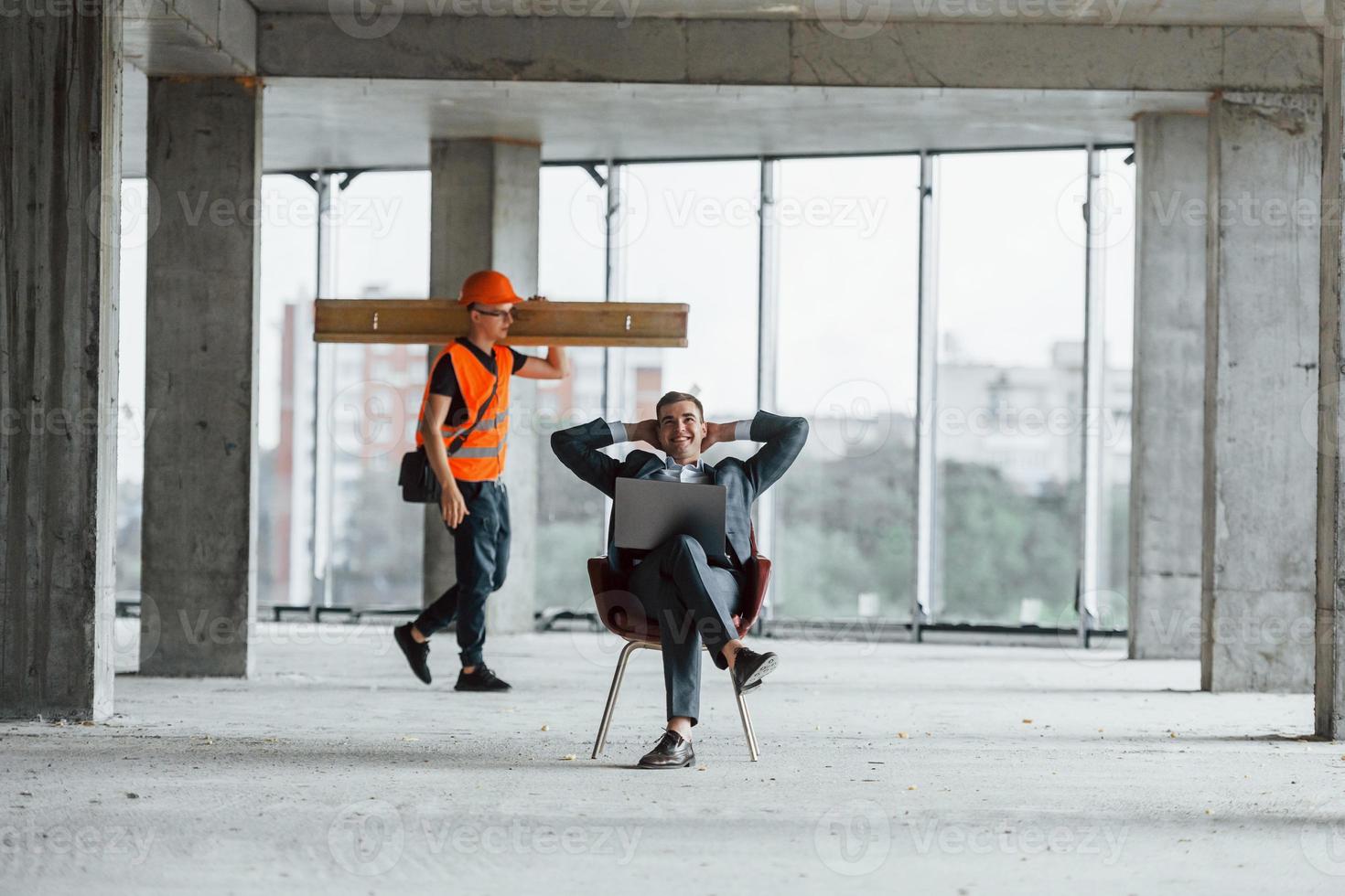 objeto em movimento. homem de terno e faz-tudo em roupas de proteção laranja está trabalhando na construção foto