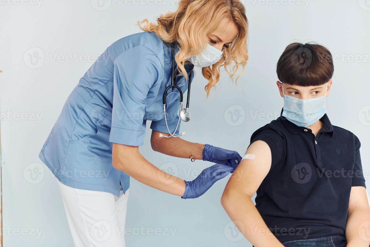 médico de uniforme fazendo vacinação para o menino de camisa preta foto