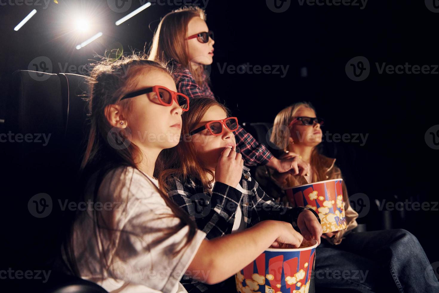 vista lateral. grupo de crianças sentadas no cinema e assistindo filme juntos foto