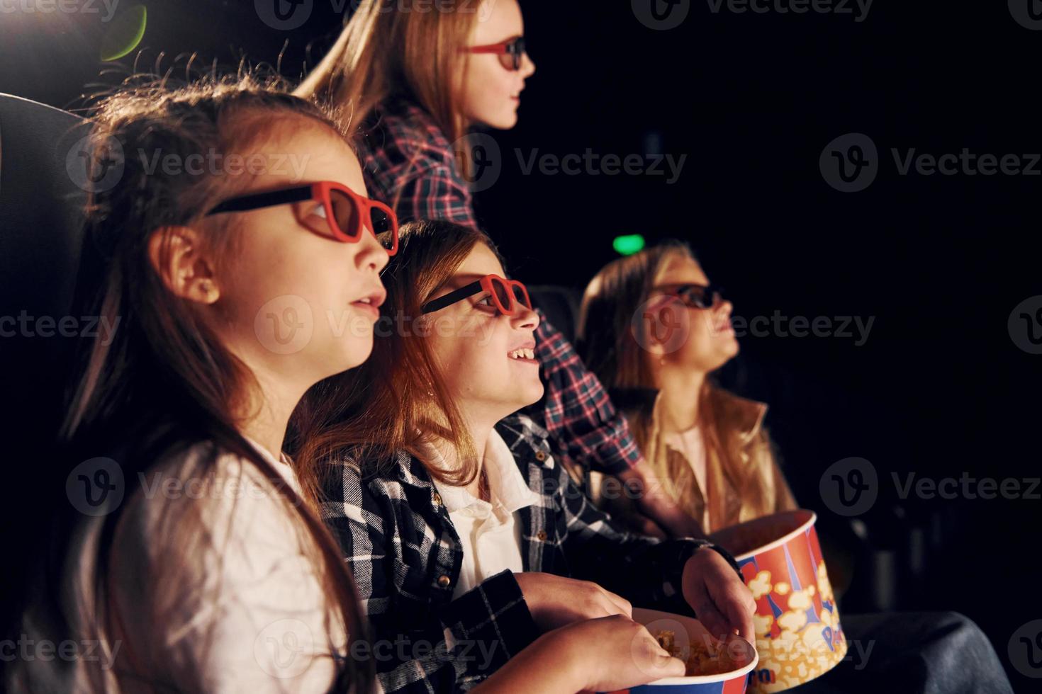 vista lateral. grupo de crianças sentadas no cinema e assistindo filme juntos foto