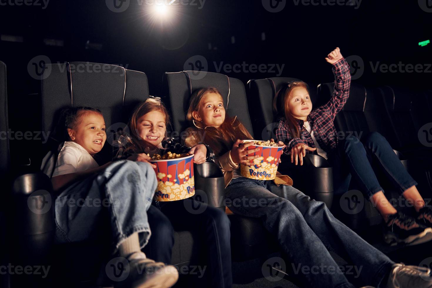 sentado nos assentos pretos. grupo de crianças sentadas no cinema e assistindo filme juntos foto