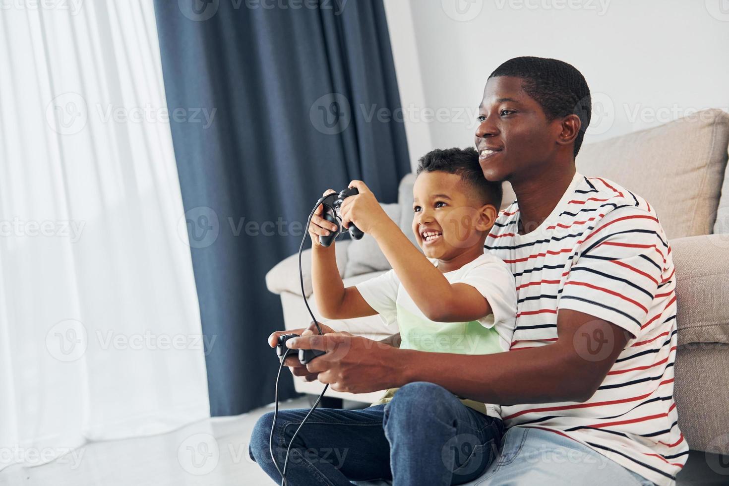 jogando video games. pai afro-americano com seu filho em casa foto