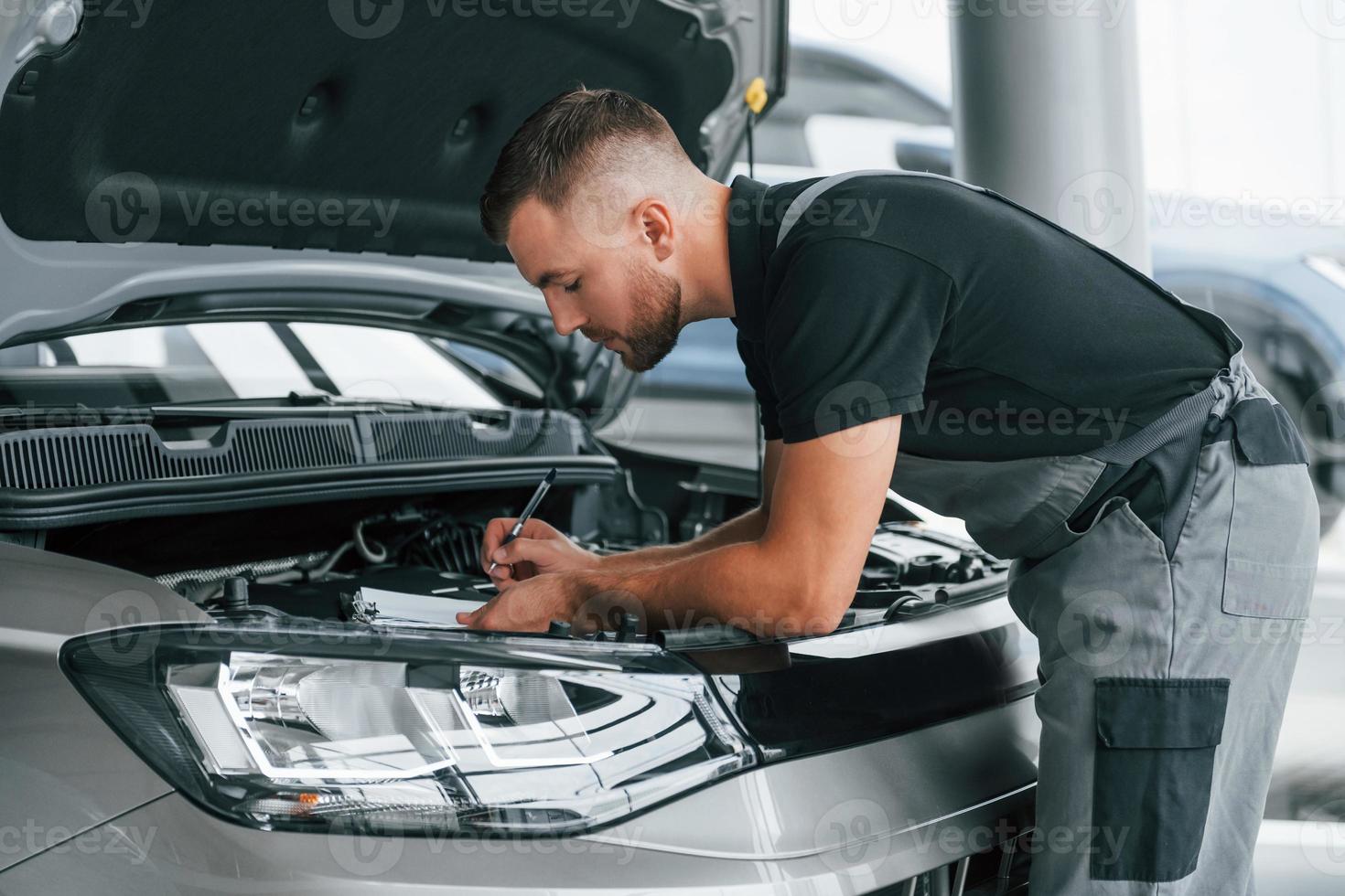 reparação do carro. homem de uniforme está trabalhando no autosalon durante o dia foto