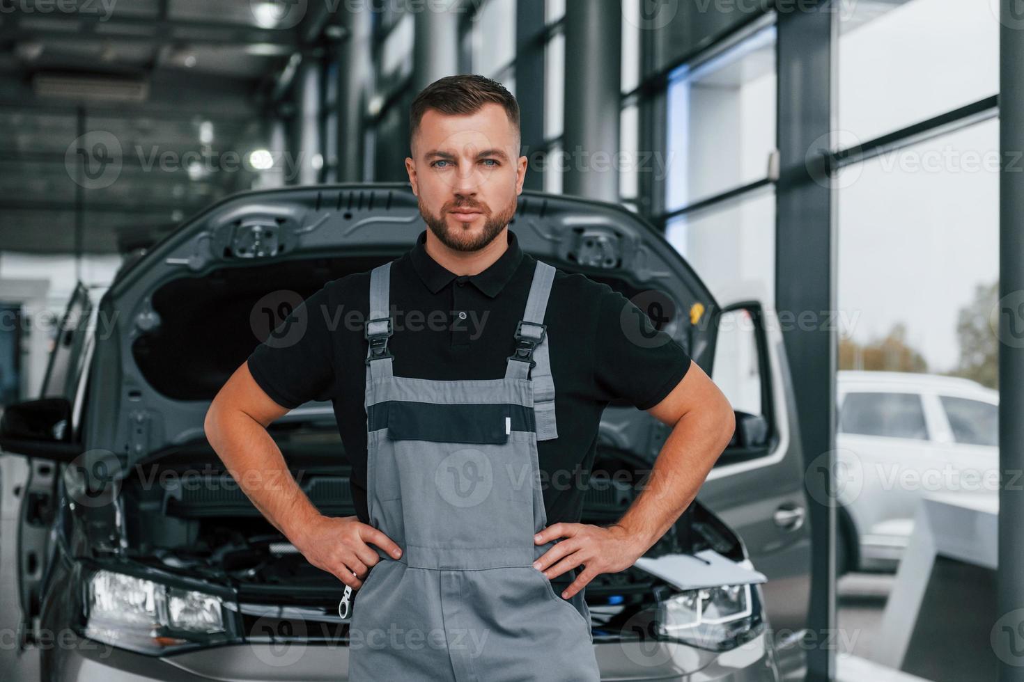 de pé contra o carro. homem de uniforme está trabalhando no autosalon durante o dia foto